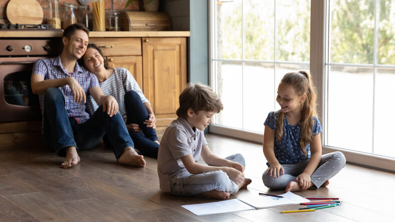 Happy family relaxing in kitchen while kids color and draw together.